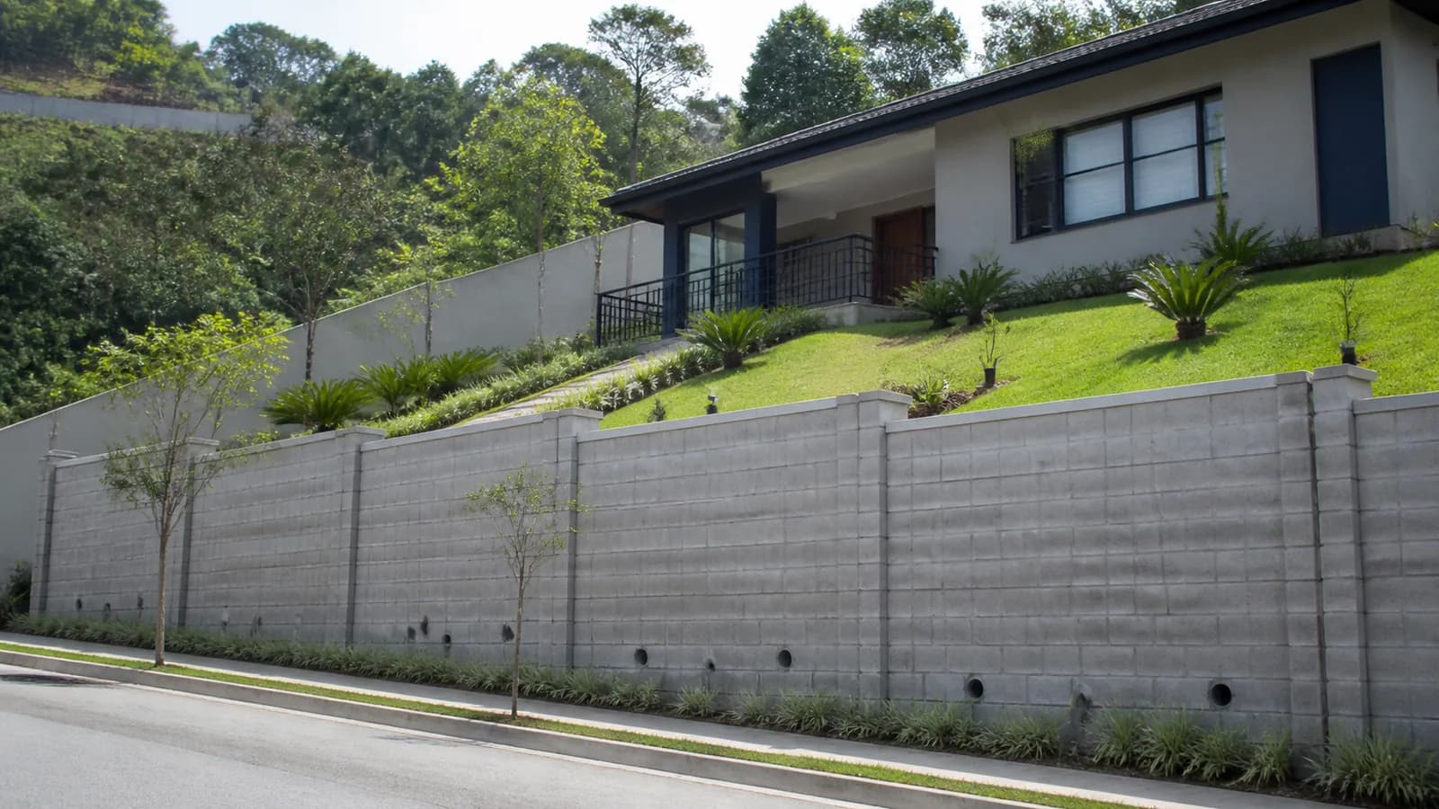 Muro de arrimo em terreno residencial inclinado com saídas de drenagem visíveis
